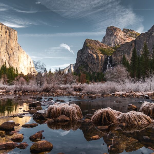 Sunset casting a warm glow on the cliffs of Yosemite National Park during a Yosemite Winter Tour, with a calm river in the foreground reflecting the serene landscape.